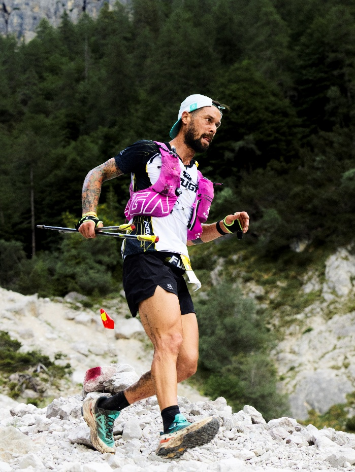 Kailas FUGA athlete powers up rocky trail in Dolomites, focused and determined, wearing pink hydration vest and trail gear.
